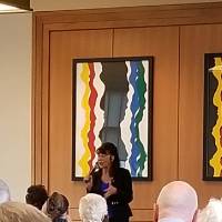 A woman with a microphone speaks to a crowd of seated people